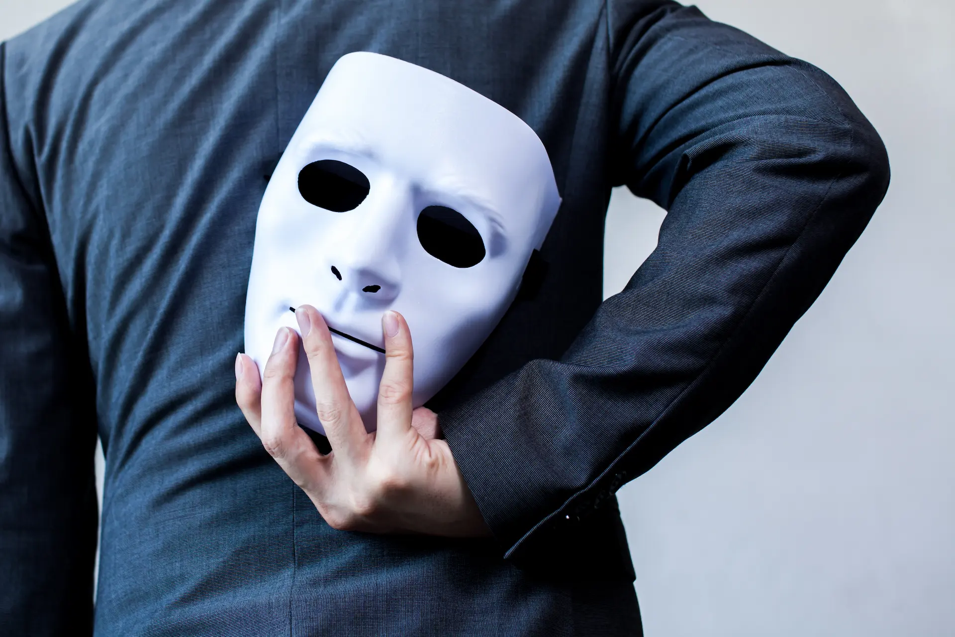 A businessman holding a mask behind his back, symbolizing hidden aspects of his true self.
