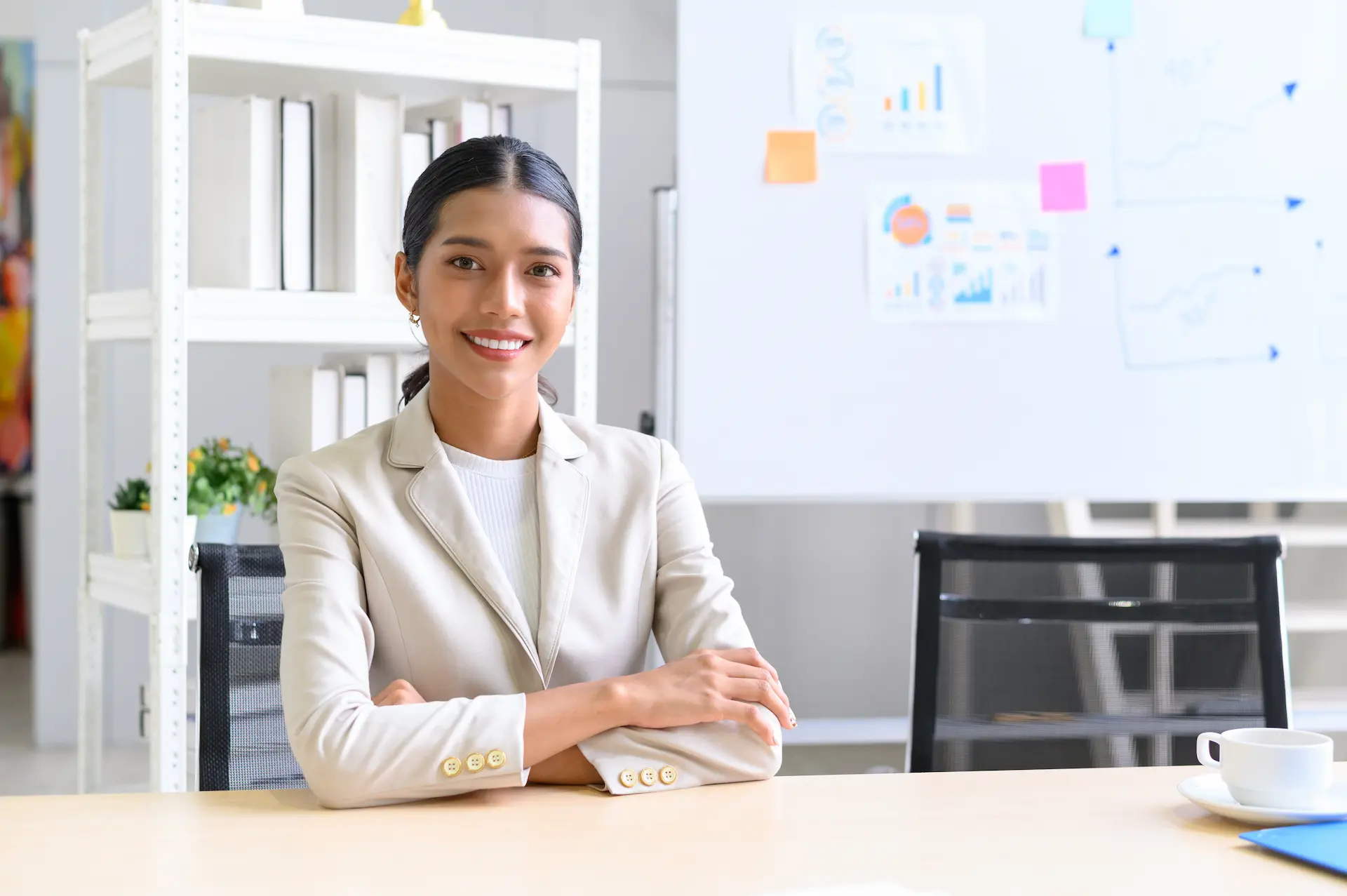 A confident professional woman sits at a desk, ready to showcase her value, with a whiteboard of charts and graphs behind her, reinforcing a business and career-focused setting.