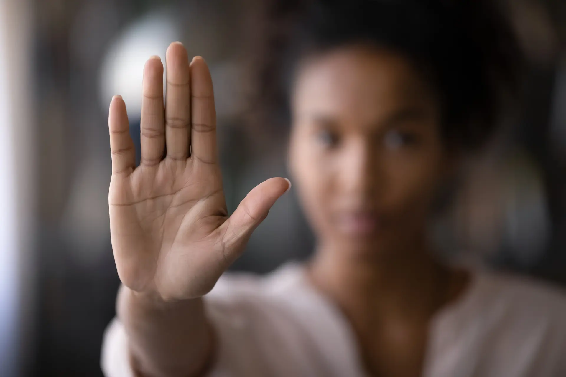 A woman raising her hand in a stop gesture, signaling her reluctance to let others see her true self and using her distance as a shield.