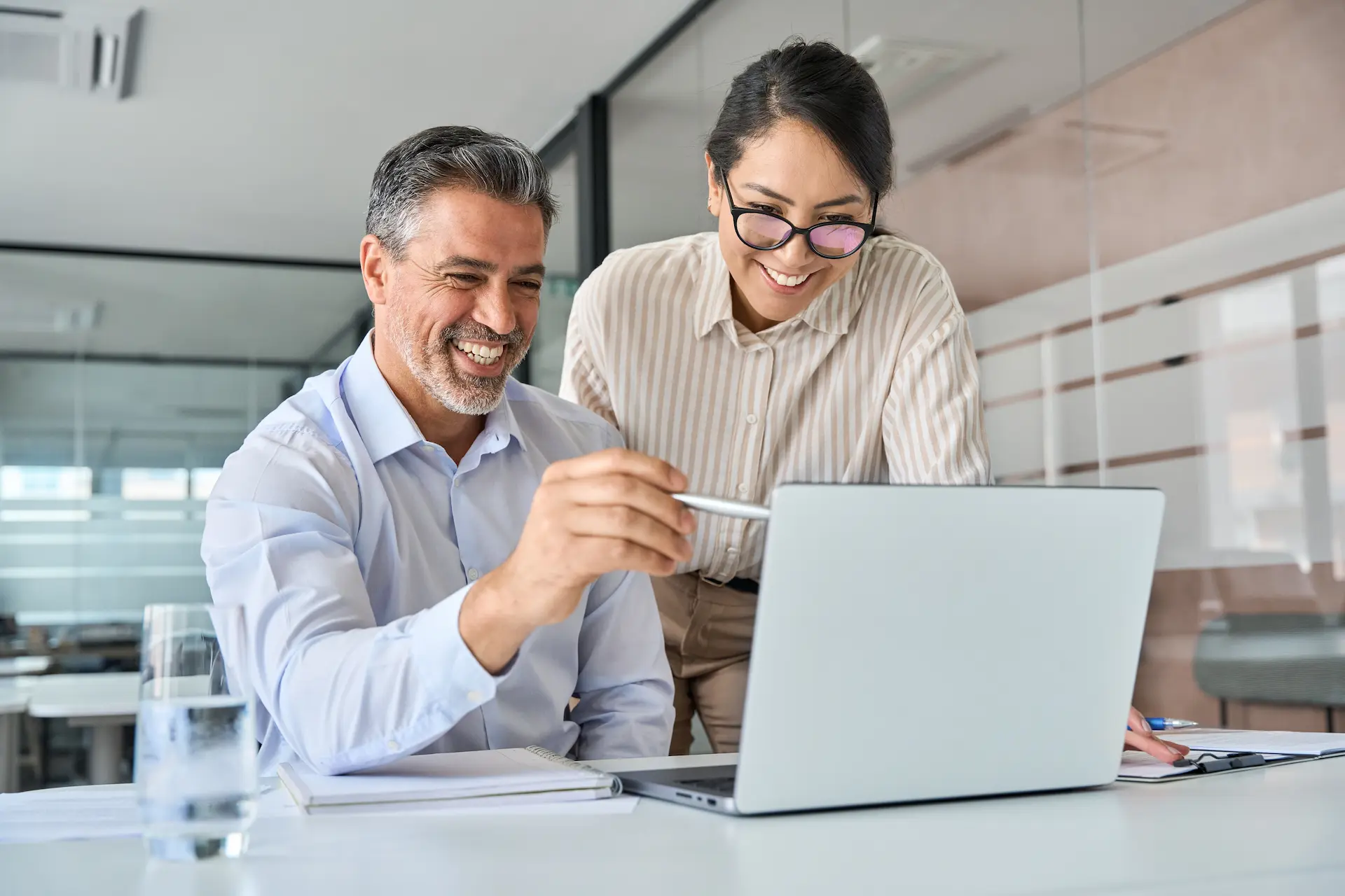 A man and woman collaborating over a laptop in an office, representing coaching leadership and knowledge sharing.