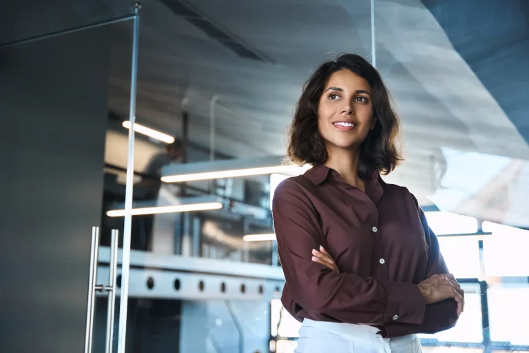 A woman stands with her arms crossed in front of an office, exuding authority, power, and confidence.