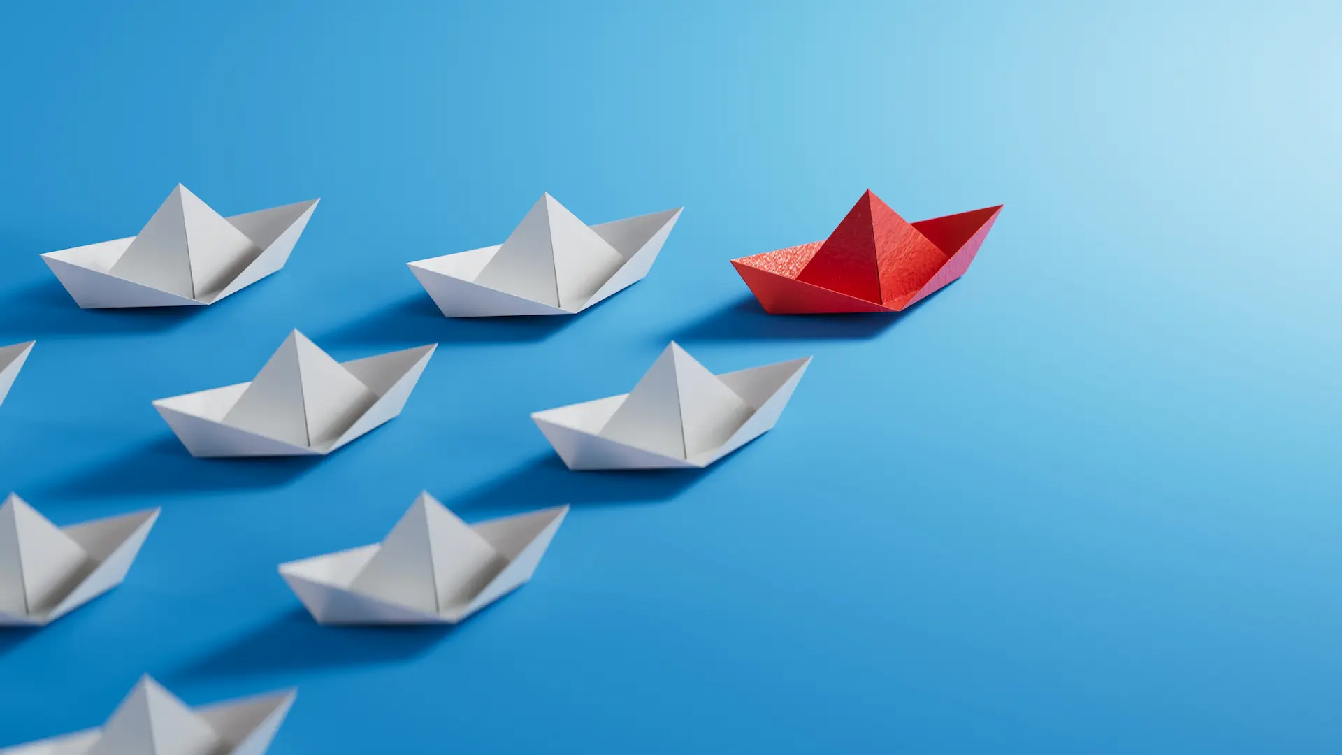 A group of white paper boats arranged in formation on a blue background, with one red paper boat leading ahead. The red boat stands out, symbolizing leadership, influence, and the power of standing apart from the crowd.