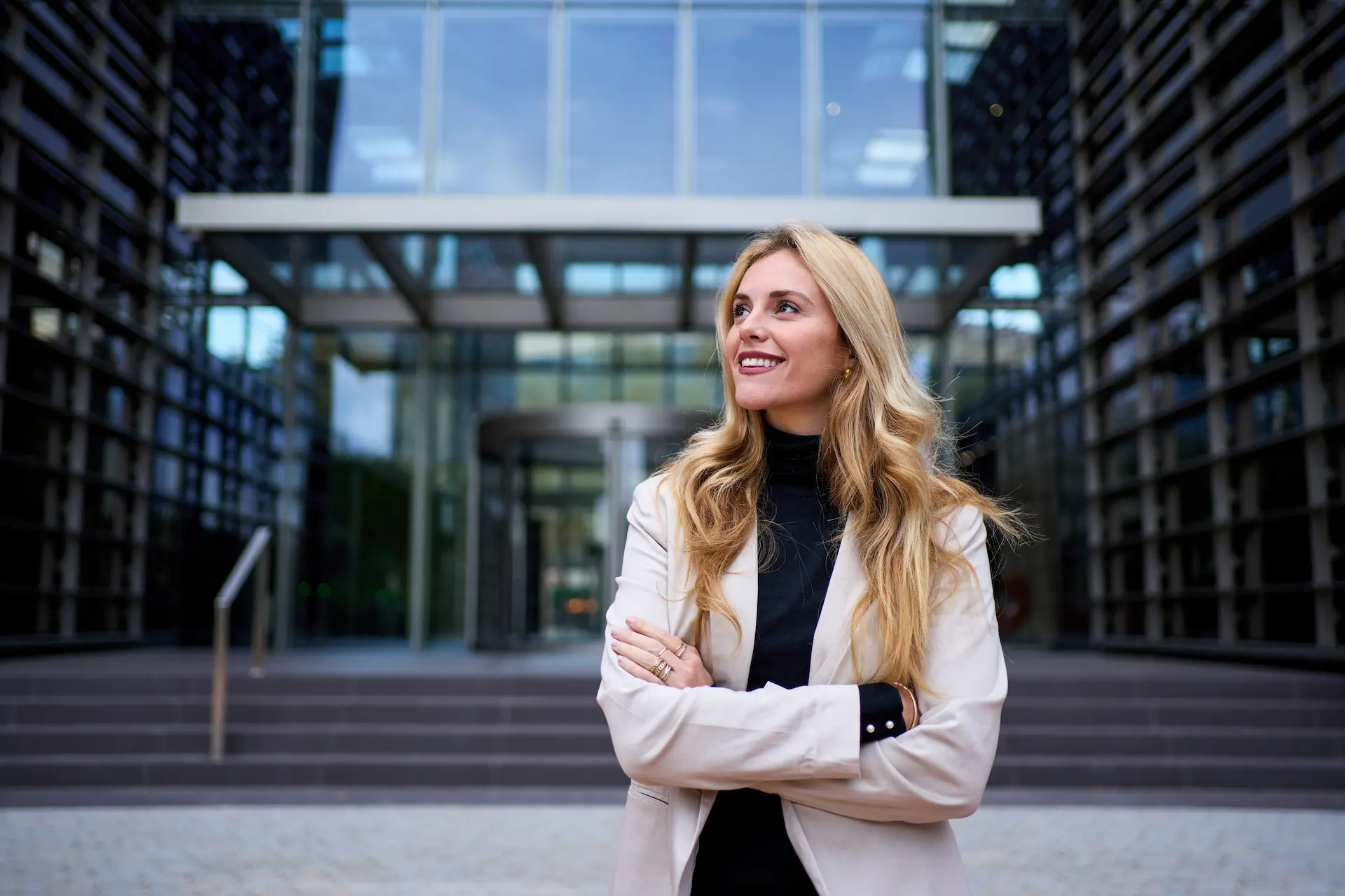 A woman standing in front of an office building with her arms crossed, showcasing a power stance and manifesting confidence.
