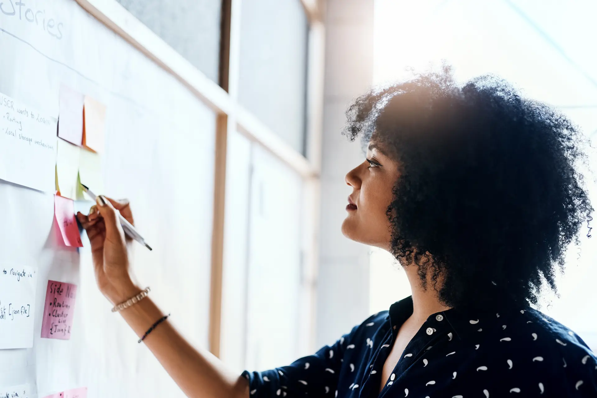 A woman writes on a whiteboard filled with notes, actively improvising and brainstorming ideas in a creative problem-solving session.