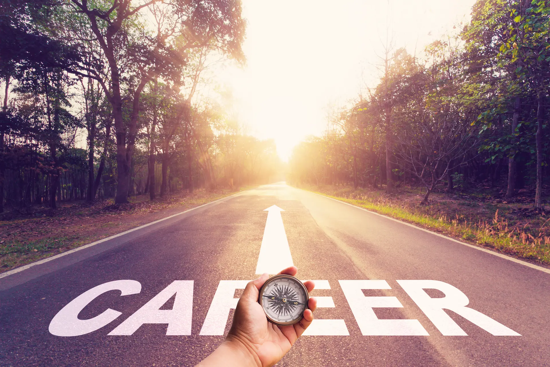 A hand holding a compass over a road with the word career painted over it, symbolizing how his values should guide his career path.