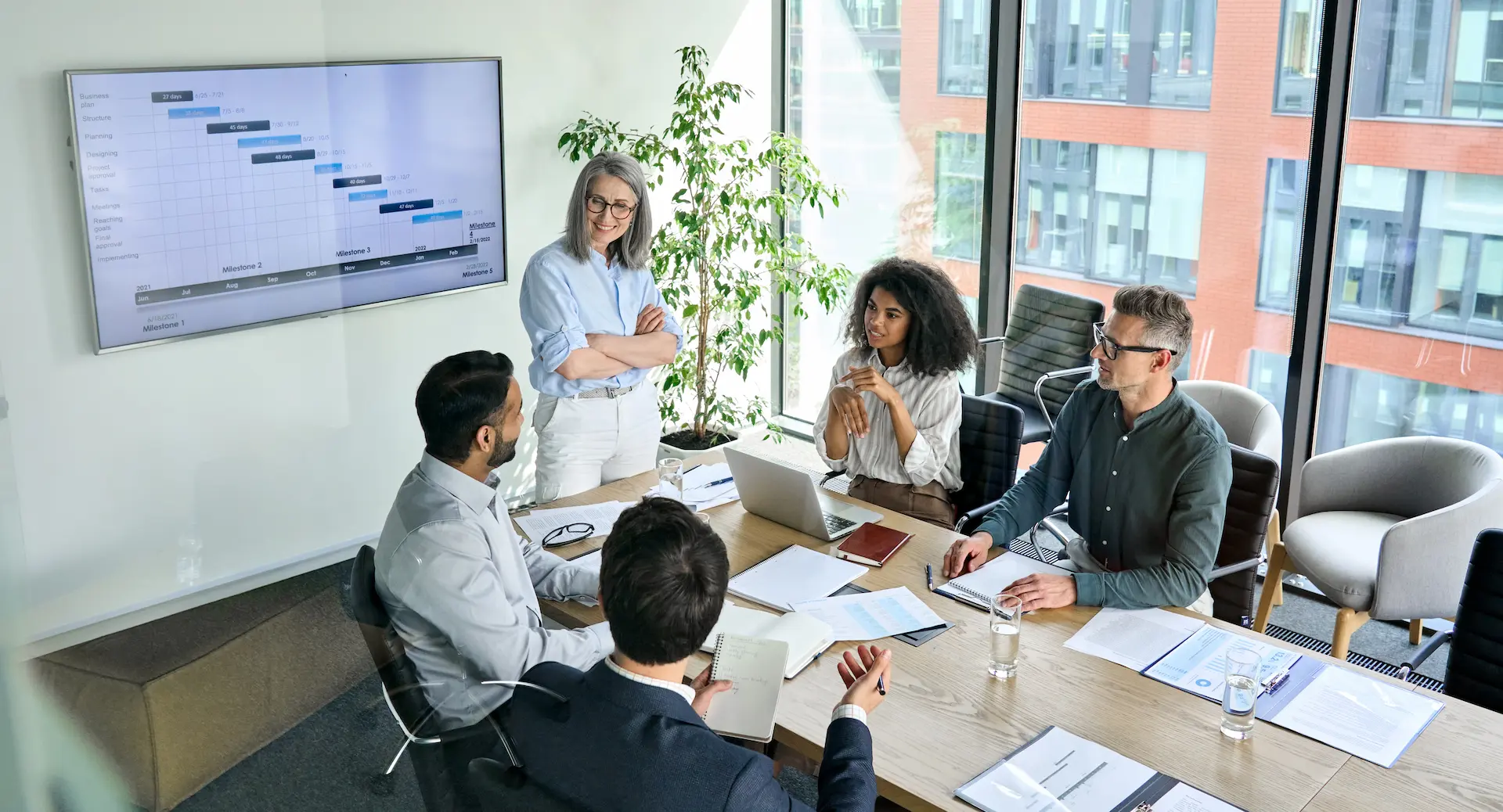 A team meeting in progress, with people gathered around a table, reviewing documents and discussing progress, showing the milestone assessment phase of project execution.
