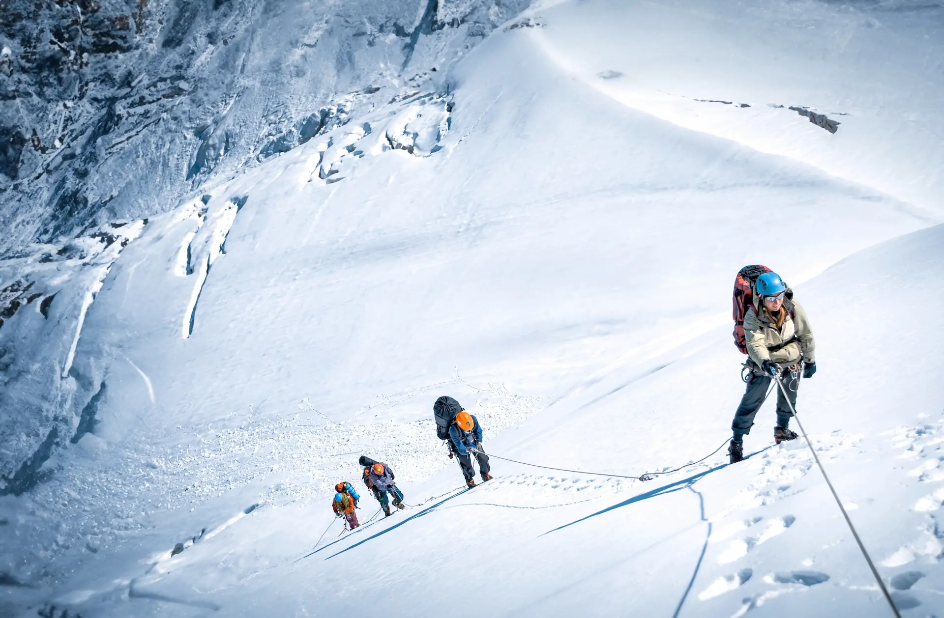 Climbers roped together ascending a steep, snowy mountain slope in harsh conditions.