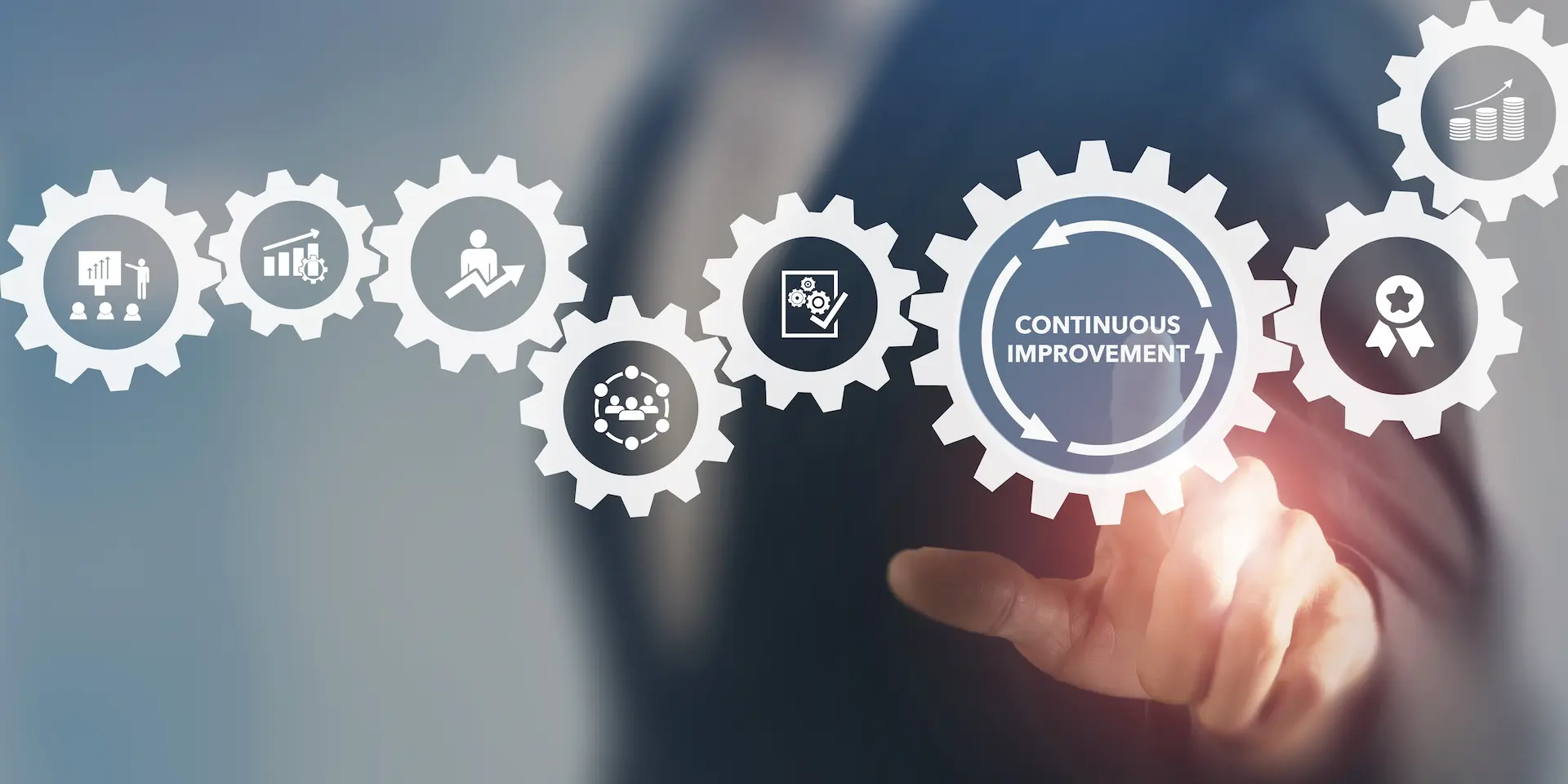 A man pointing to a gear with the words "continuous improvement" in a network of interlocking gears, symbolizing lean efforts to eliminate waste through ongoing optimization.