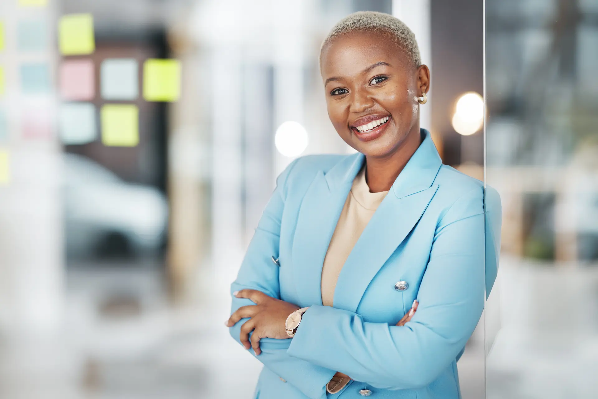 A confident woman leaning against a wall in a modern office, embodying a lean mindset that values clarity and eliminates workplace waste.