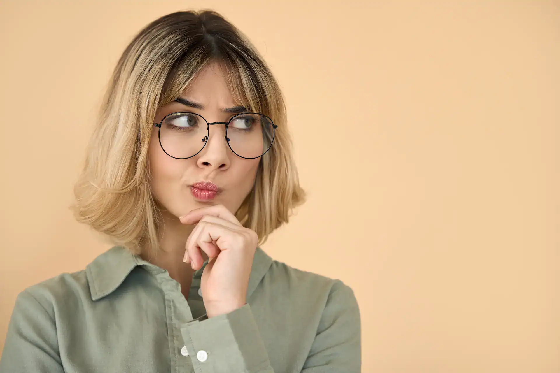 Thoughtful woman with glasses pondering a decision against a neutral background.