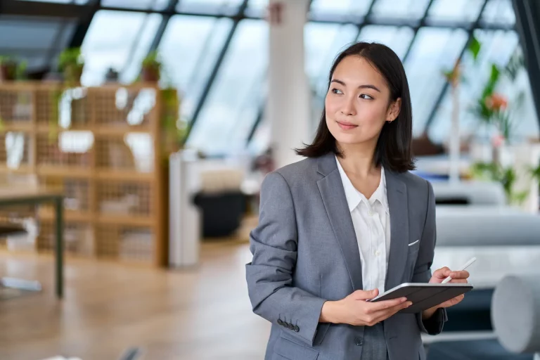 A manager stands in her office holding an iPad, reviewing her team’s project plans.