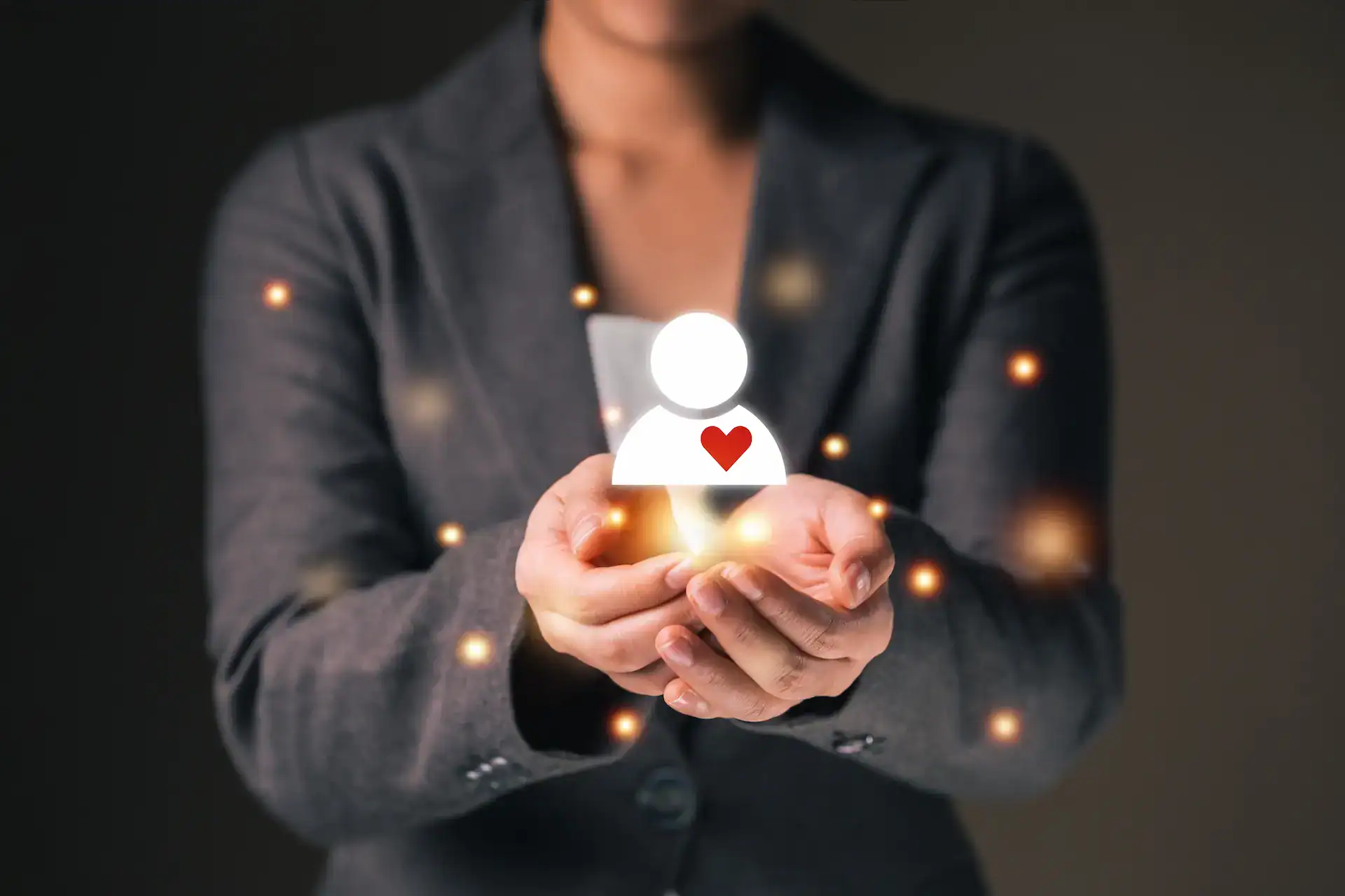 A person in a suit holding a glowing icon of a figure with a heart on its chest, surrounded by soft light particles, symbolizing personal growth, care, and intentional skill development.