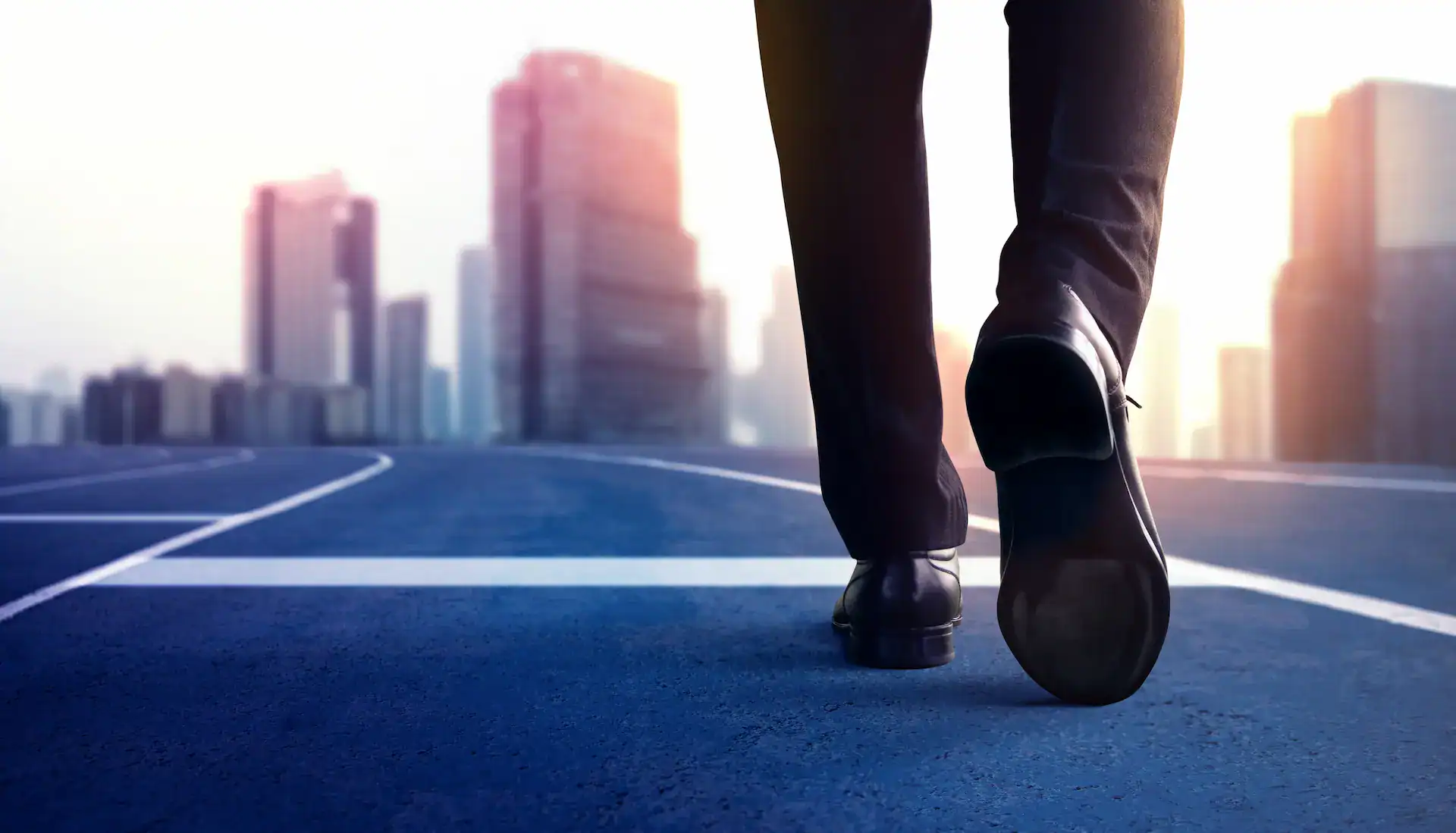 A man's feet in formal shoes, walking towards a city, symbolizing walking towards the future.
