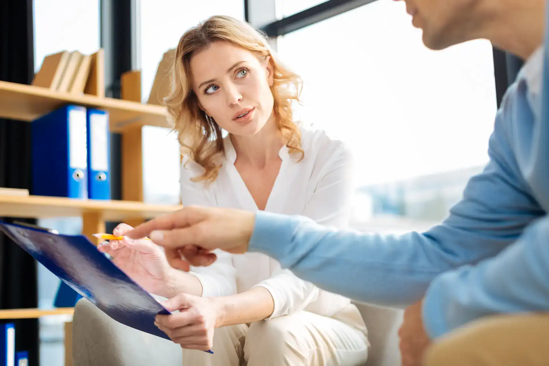 A woman attentively listening to a man while holding a clipboard, suggesting a thoughtful discussion or mentoring session, symbolizing how combining different skills can support communication, collaboration, and professional growth.