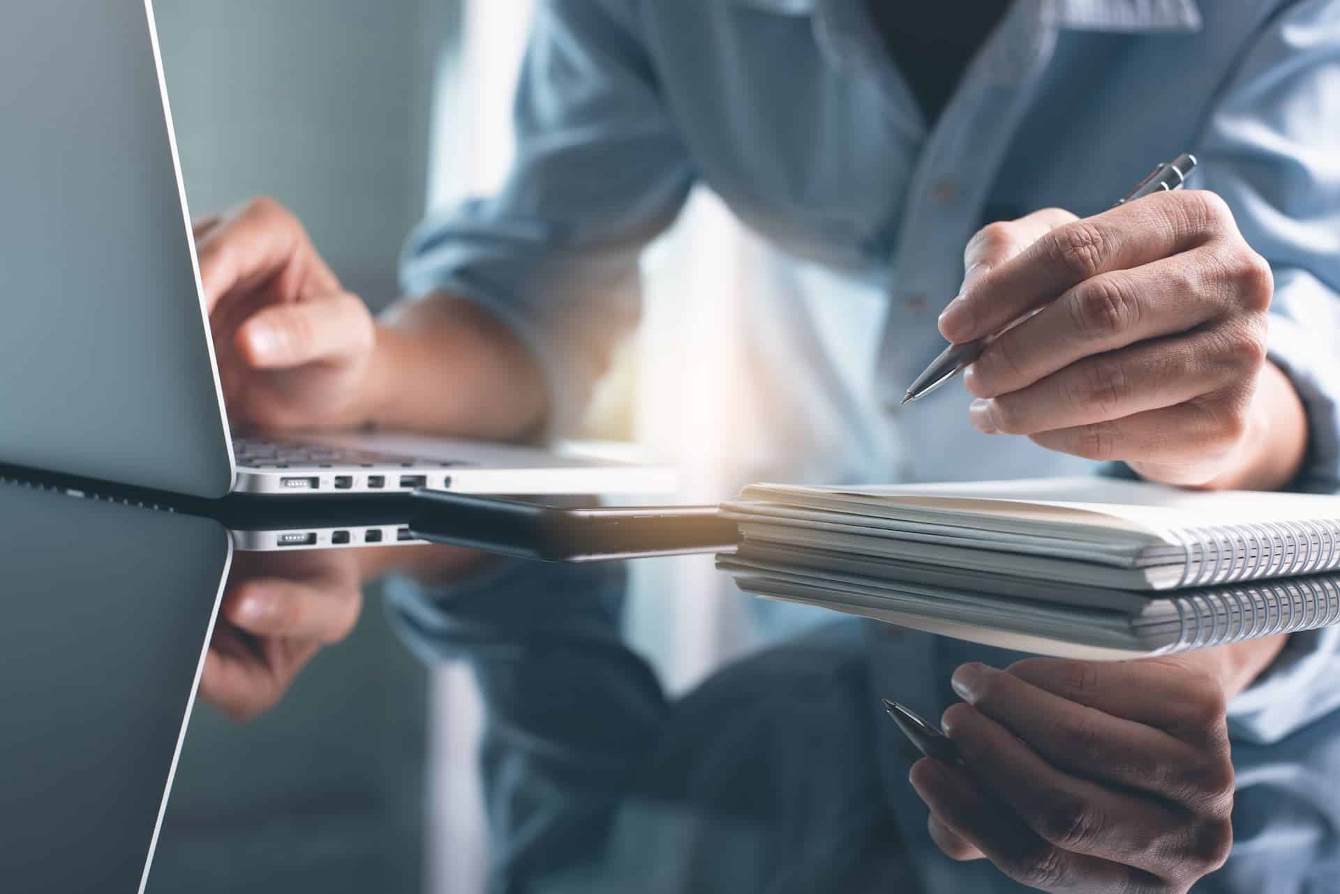 A close-up of someone developing a personal learning agenda while multitasking on a laptop.