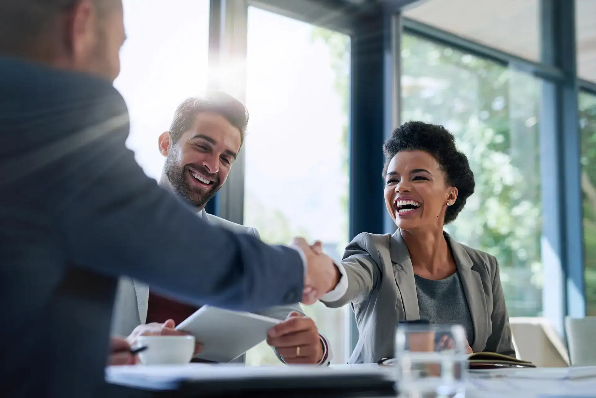 A woman laughs and shakes hands with a man in a meeting, showing mutual support and allyship.