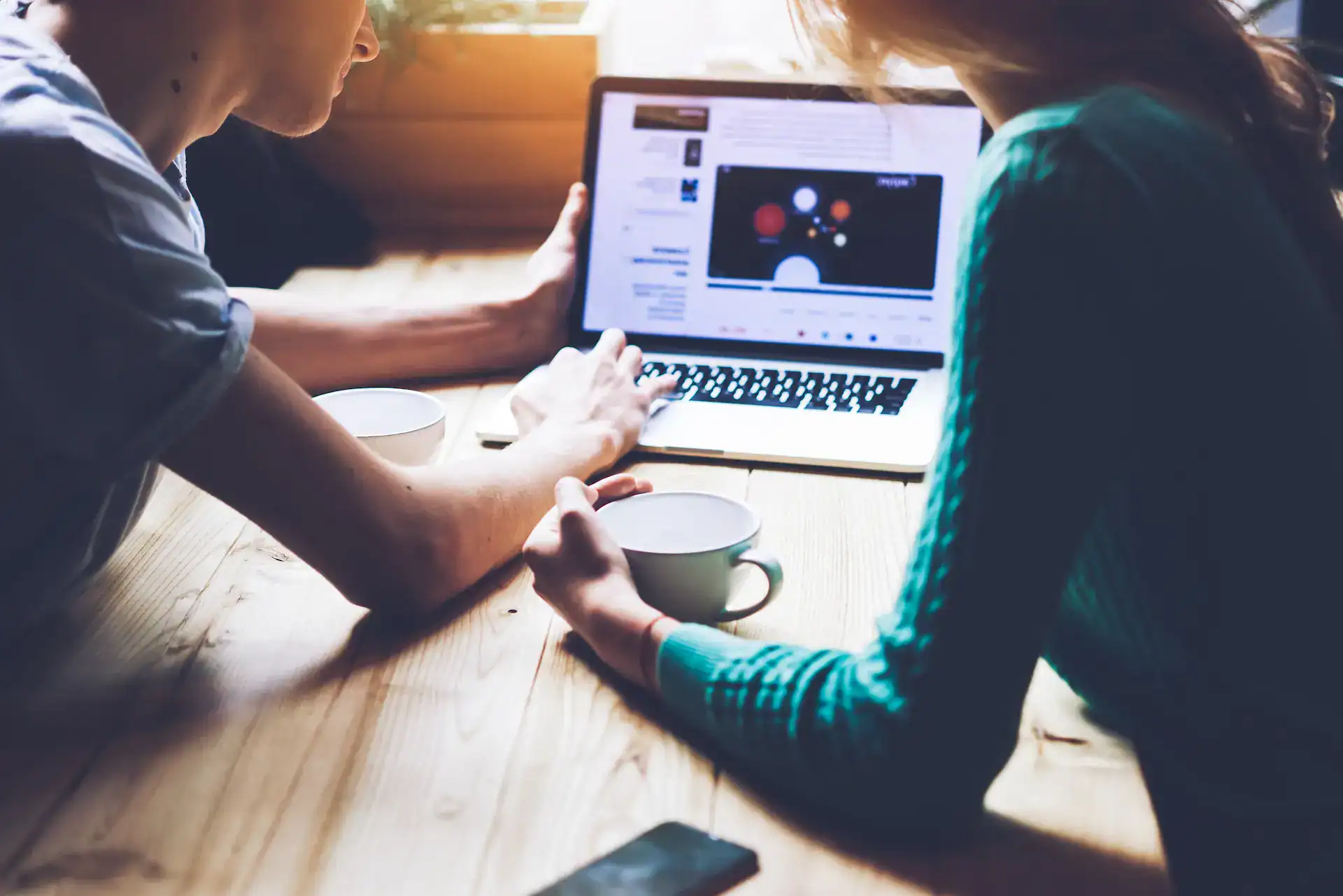 Two people sitting over a laptop as one helps the other build a strong LinkedIn profile.