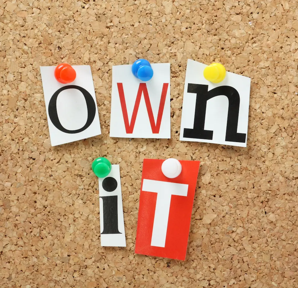 Cut-out letters pinned to a corkboard spelling “own it,” representing workplace ownership.