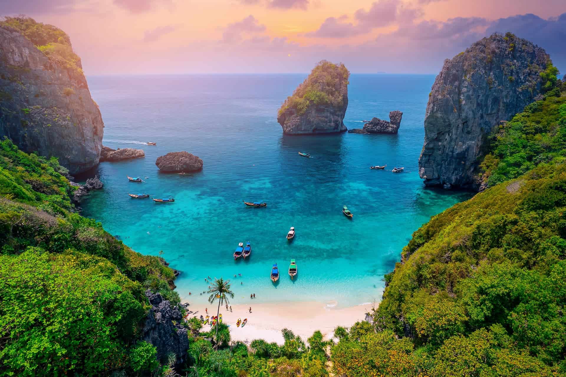 Tropical beach with turquoise water, boats anchored in a sheltered cove, and lush green cliffs — a peaceful setting perfect for truly unplugging on vacation.