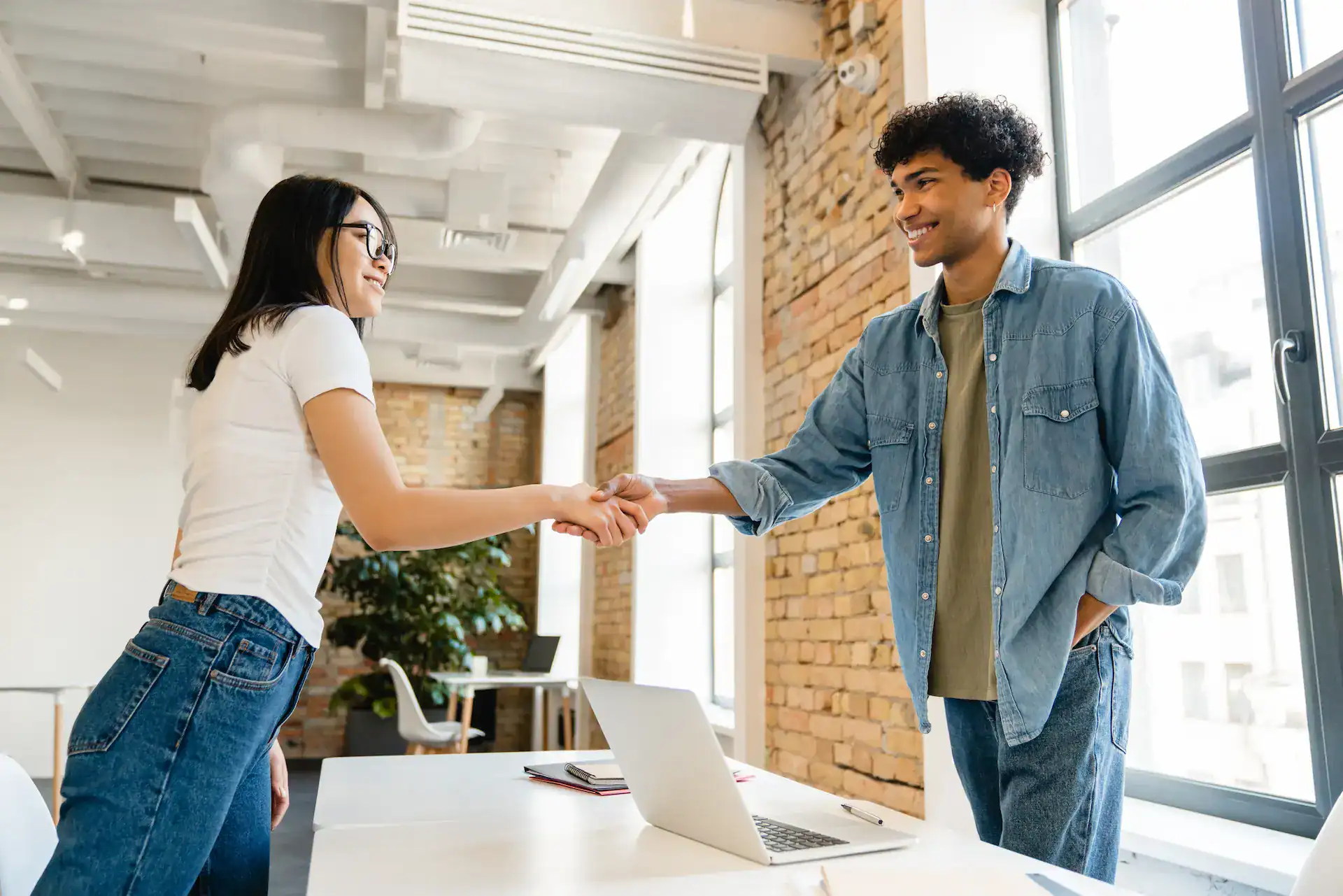 Two young professionals shake hands in a modern office, representing a moment of mutual respect, appreciation, recognition, and acknowledgment.