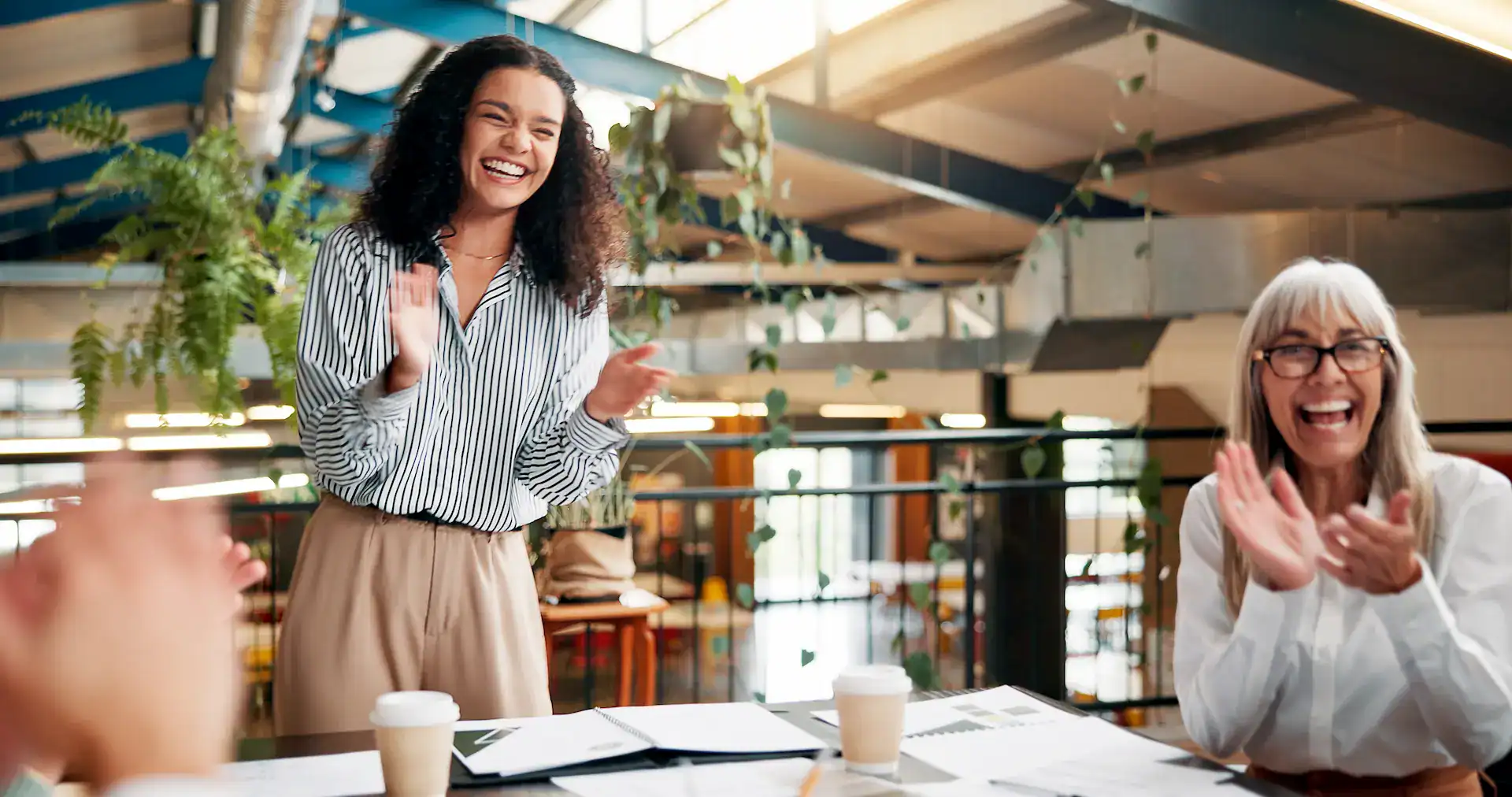 Two women are enthusiastically clapping and smiling in a meeting, demonstrating active appreciation and peer recognition.