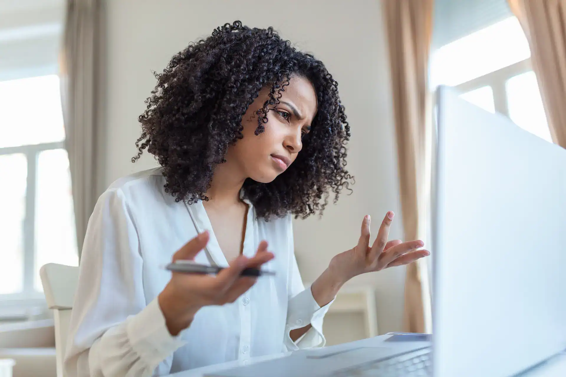 A perplexed woman holding a pen looks at her laptop, seemingly struggling to understand her role.