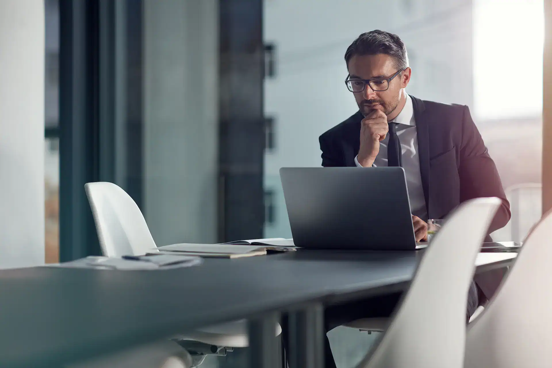 A professional man sitting at a conference table looks at his laptop with a thoughtful expression, embodying how values guide decision-making.