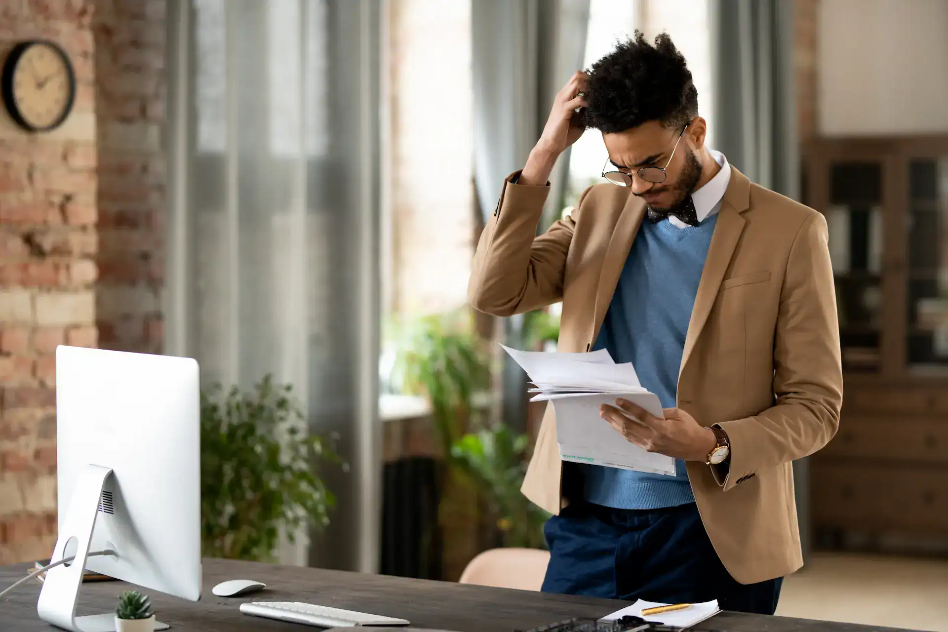A confused man looks at documents while scratching his head, possibly struggling to understand his role.