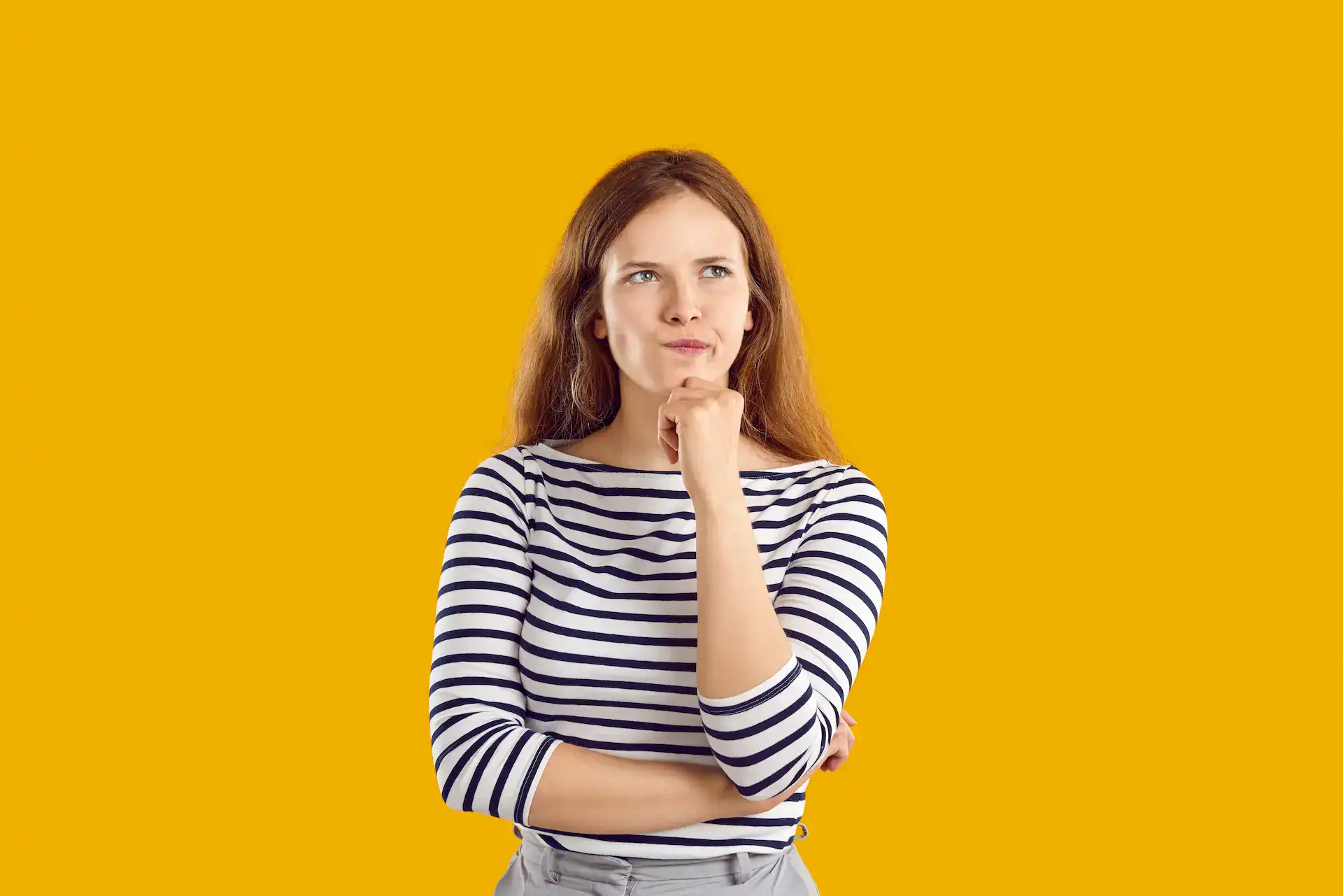A woman with a pensive expression, her chin resting on her hand, stands against a bright yellow background, questioning her decisions against her values.