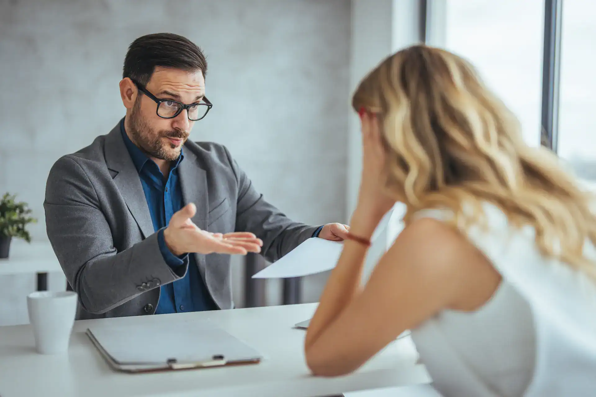 Male manager gesturing while frustrated female employee listens during tense office discussion.