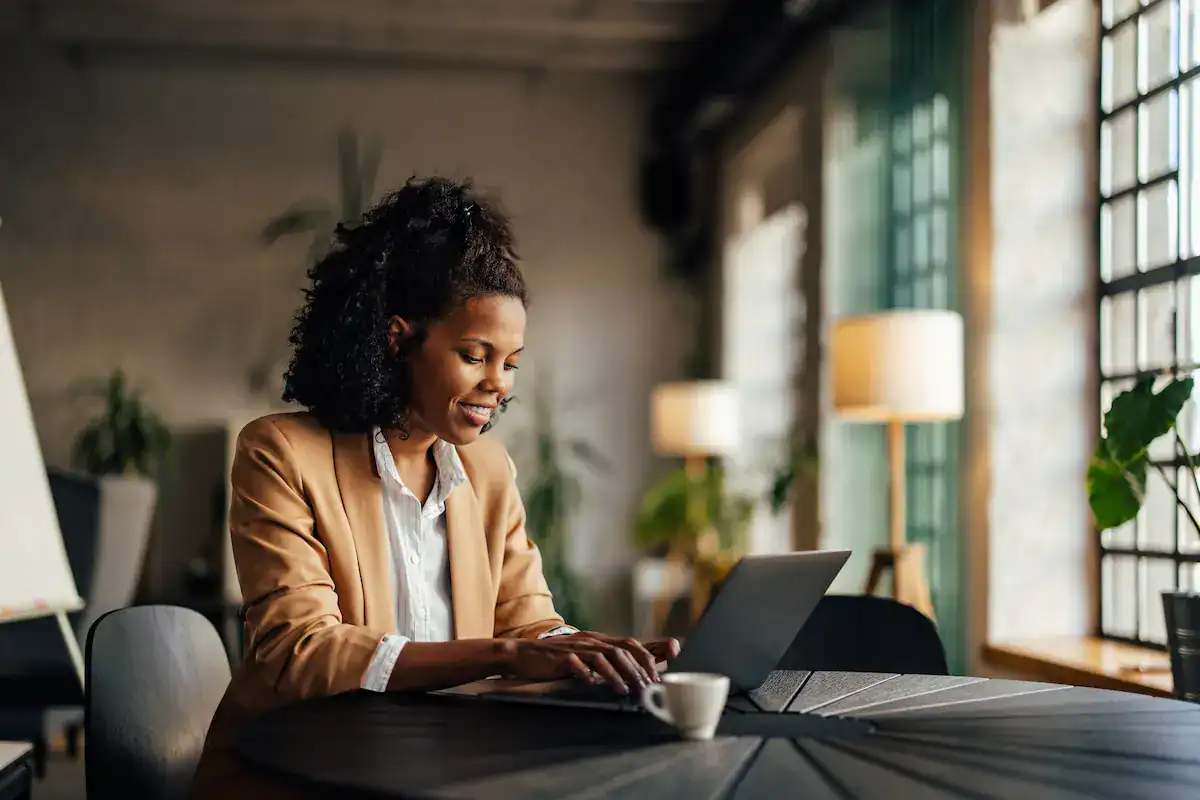 A professional woman smiling while using a laptop at a table, showing her engagement in a task with clear expectations.