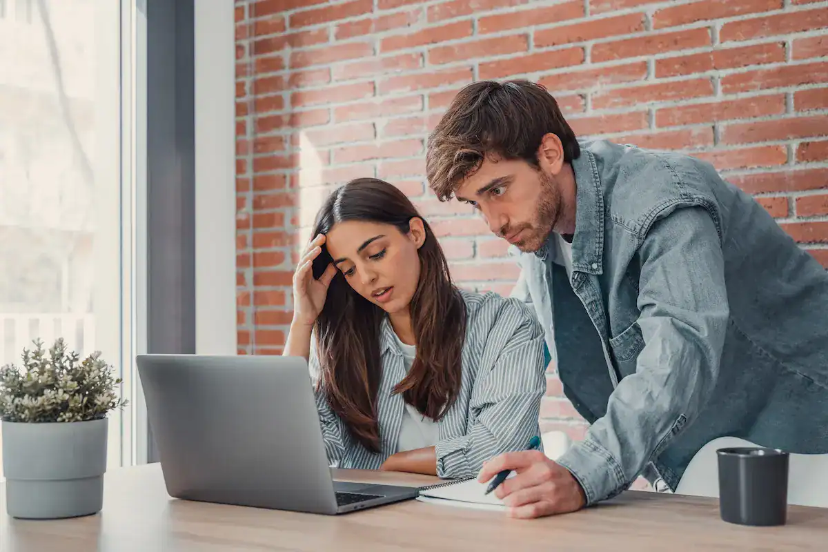 Two colleagues discuss a project on a laptop, showing frustration as they lack clear expectations.