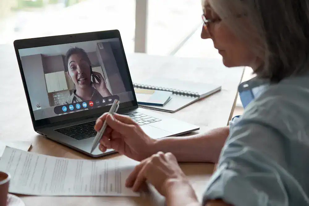 A woman on a video call reviews paperwork related to the hiring process.