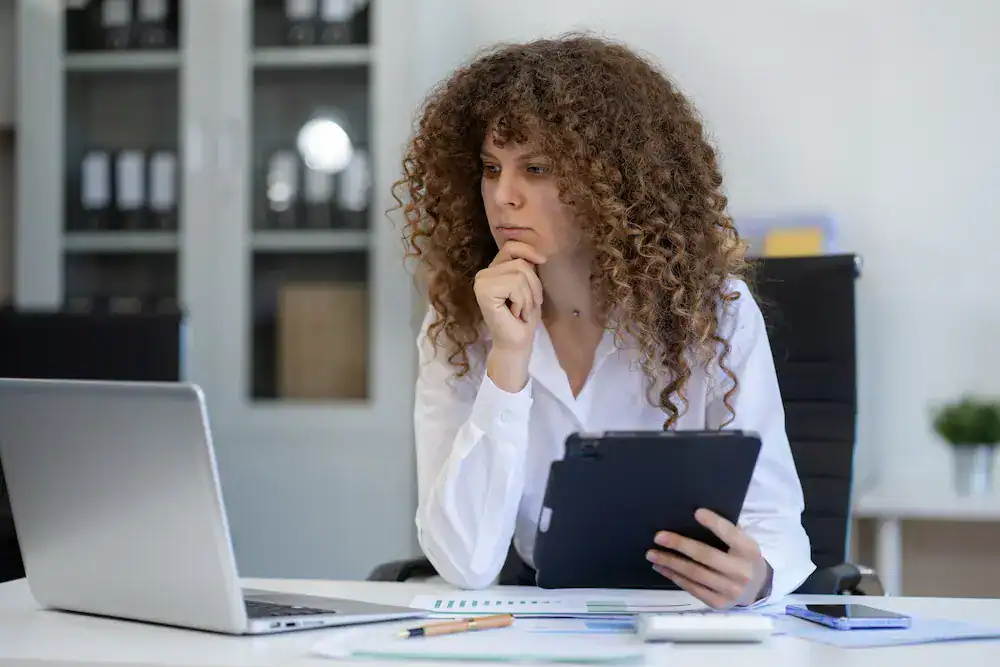 A woman at her desk works on a tablet and laptop, symbolizing a person problem-solving to overcome recent mistakes.
