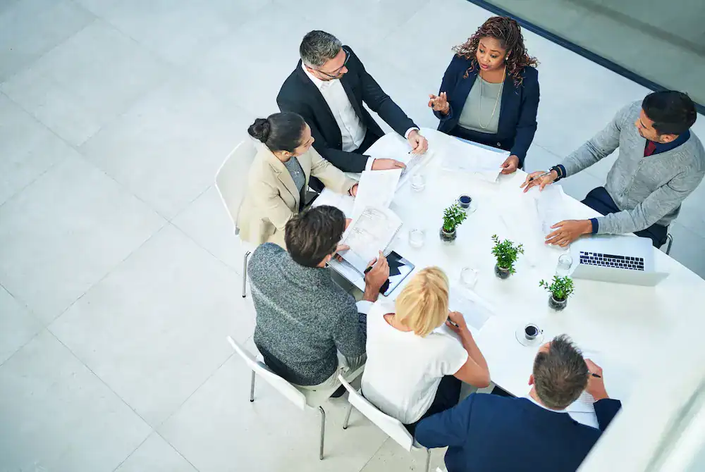 A diverse group of people sits around a conference table discussing how to learn from collective setbacks and mistakes.