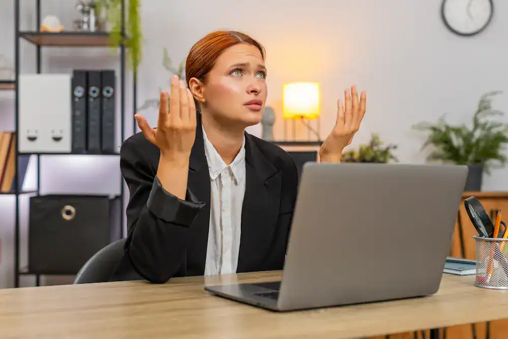 A woman at her desk looks confused with her hands up, demonstrating the common feeling of bewilderment after mistakes happen.