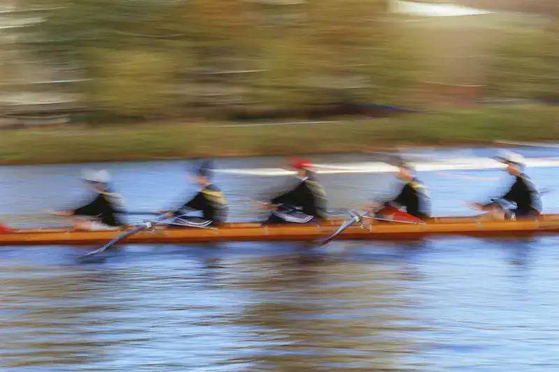 Blurred rowing team moving in unison on a river, symbolizing coordination, speed, and teamwork.