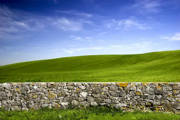 Low stone wall dividing green grass and rolling hills under a blue sky, representing healthy personal boundaries.