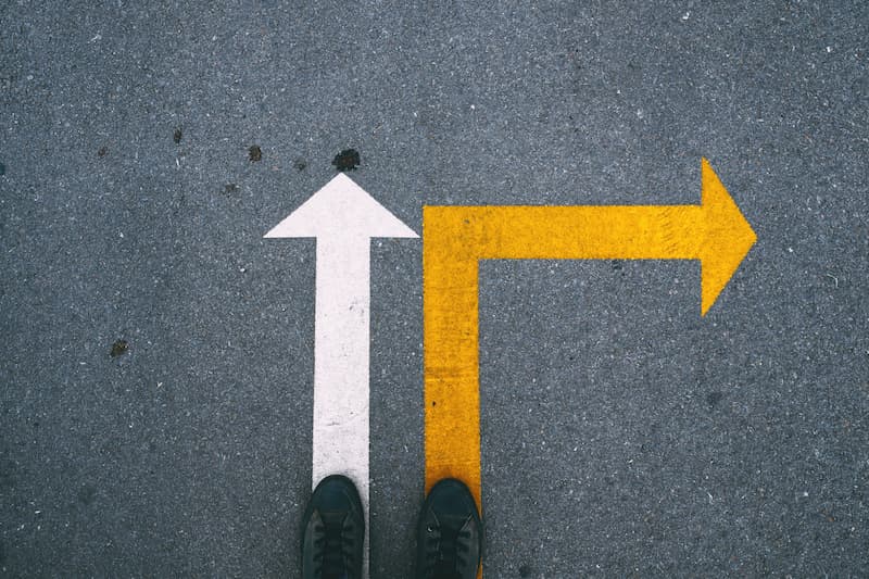 Person standing at a fork in the road with arrows pointing straight ahead and to the right, symbolizing a career decision.