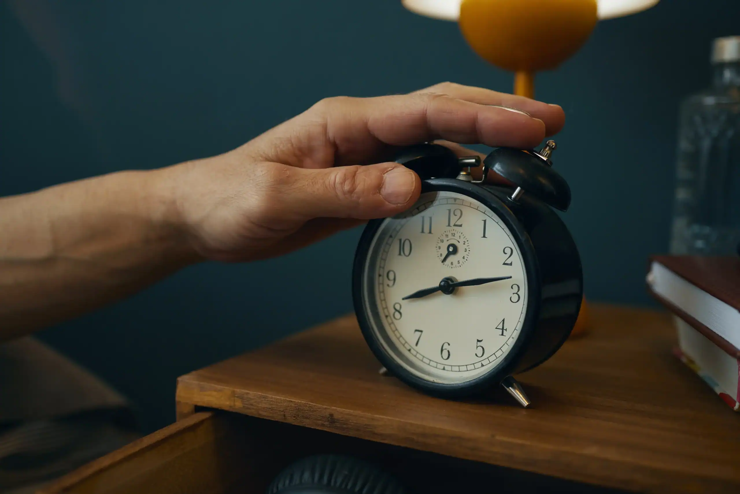 A hand reaching to turn off an alarm clock on a bedside table, symbolizing a moment of decision and taking control of one’s career.