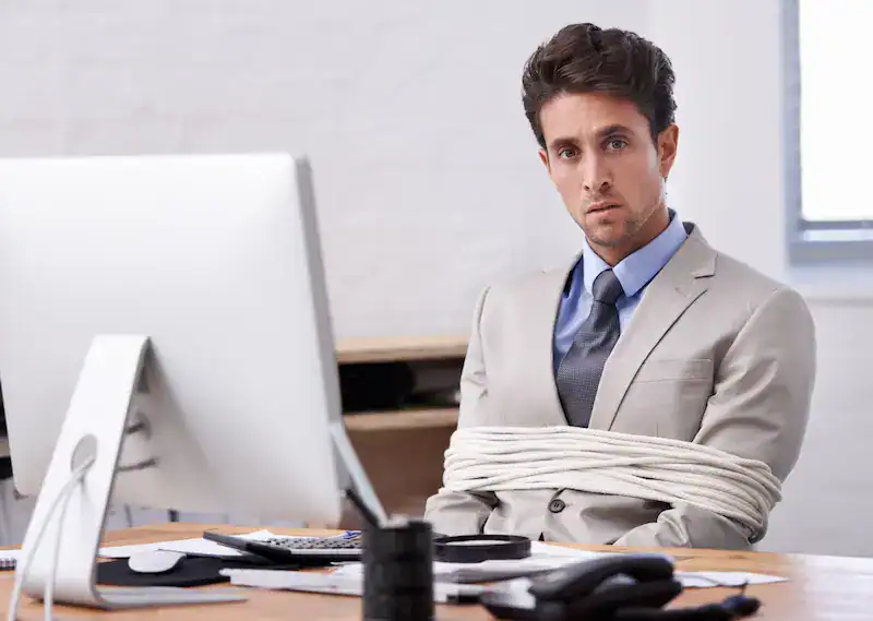 Professional tied to a desk at work, symbolizing feeling stuck and constrained in a career.