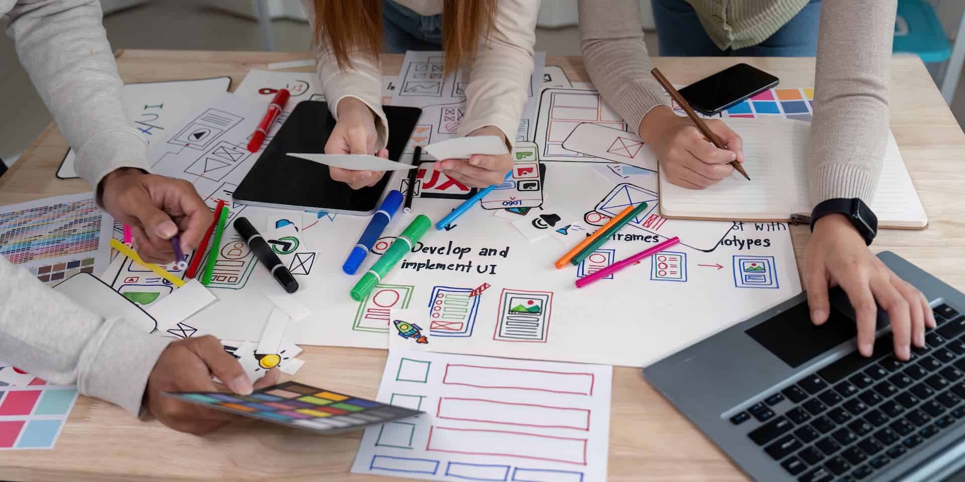 Hands of a team gathered over a table filled with papers and designs, actively prototyping concepts for a new project.