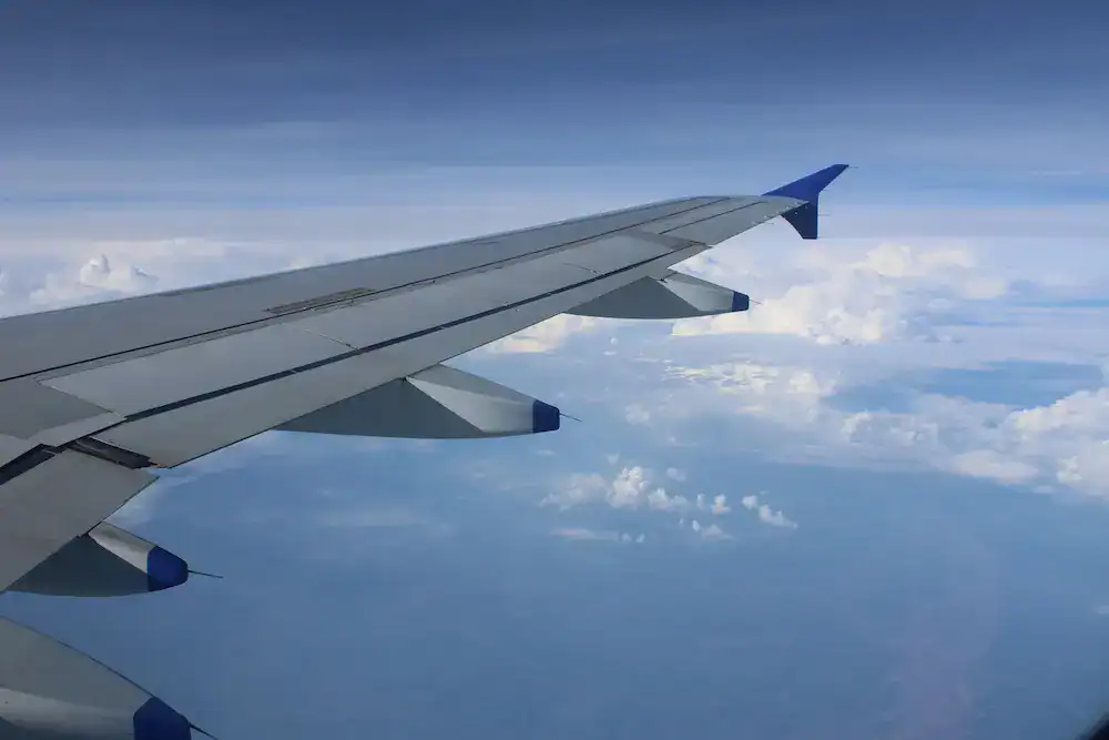 View from an airplane window showing a wing above the clouds mid-flight, symbolizing perspective and transition.