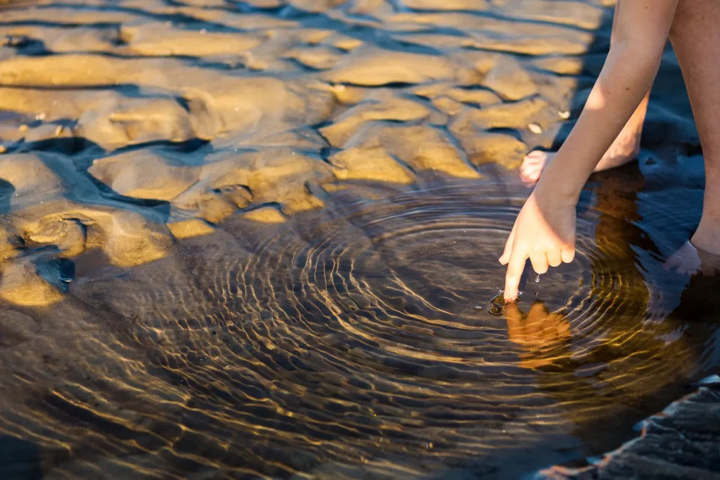 Hand touching water and creating ripples, symbolizing how small actions can create a wider impact on others.