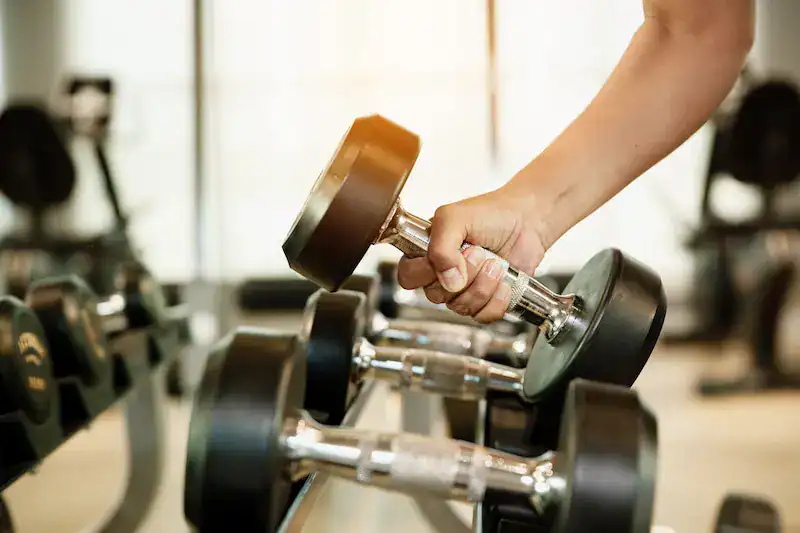 Person lifting a dumbbell in a gym, representing building strengths, growth, and professional development over time.