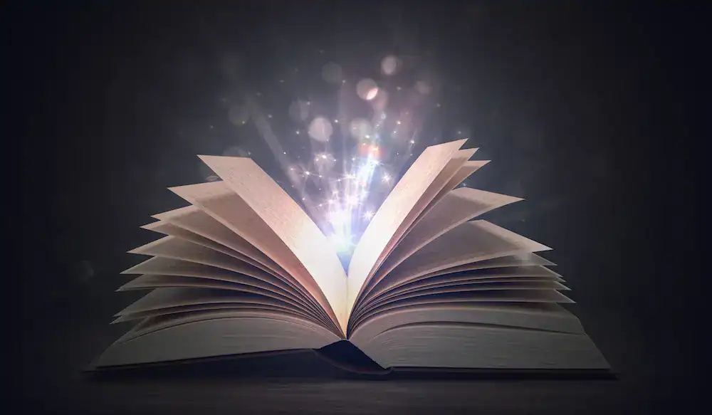 Open book with glowing light rising from its pages, symbolizing the stories, assumptions, and narratives we create in our minds.