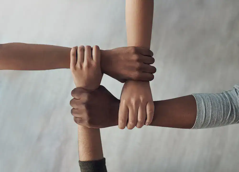 Four people holding one another’s arms to form a square, representing trust, reliability, and support among colleagues at work.